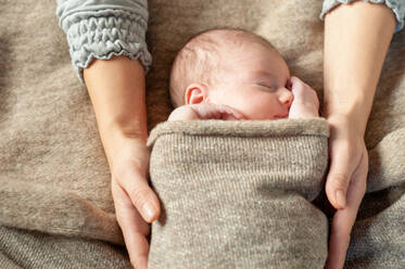 Ein vier Wochen altes Baby, eingewickelt in eine braune Decke, wird von seiner Mutter gehalten und schläft. - CUF55558