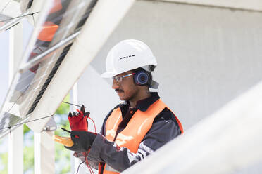 Männlicher Ingenieur mit Schutzhelm und Gehörschutz bei der Arbeit auf einer Baustelle. - CUF55565