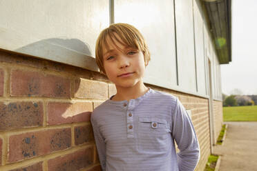 Porträt eines Jungen mit brünettem Haar, der sich an eine Backsteinmauer lehnt und in die Kamera schaut. - CUF55577