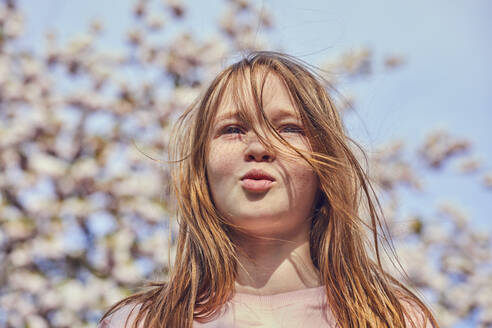 Porträt eines brünetten Mädchens, das im Freien steht, Baum mit rosa Blüten im Hintergrund. - CUF55582