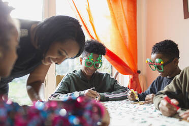 Glückliche, festliche Familie beim Verzieren von Weihnachtsplätzchen am Tisch - CAIF28155