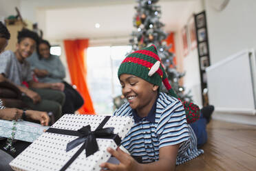 Glücklicher Junge öffnet Weihnachtsgeschenk auf dem Wohnzimmerboden - CAIF28163