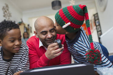 Glücklicher Sohn küsst Vater beim Öffnen des Weihnachtsgeschenks - CAIF28171