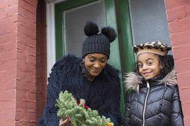Glückliche Mutter und Tochter mit Weihnachtskranz auf der Treppe vor dem Haus - CAIF28175