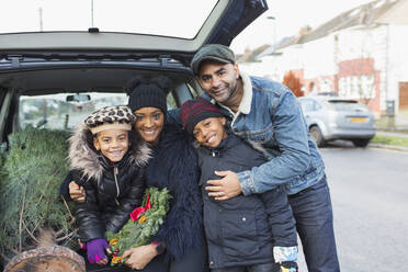 Porträt einer glücklichen Familie, die einen Weihnachtsbaum in den Kofferraum eines Autos lädt - CAIF28179