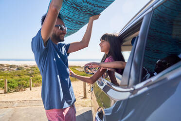Tochter sieht zu, wie ihr Vater am sonnigen Strand das Surfbrett aus dem Auto nimmt - CAIF28211