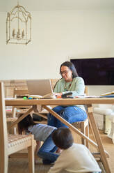 Kinder spielen unter dem Tisch, während die Mutter am Laptop arbeitet - CAIF28237