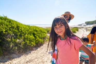 Portrait glückliches Mädchen am sonnigen Strand mit Familie - CAIF28242