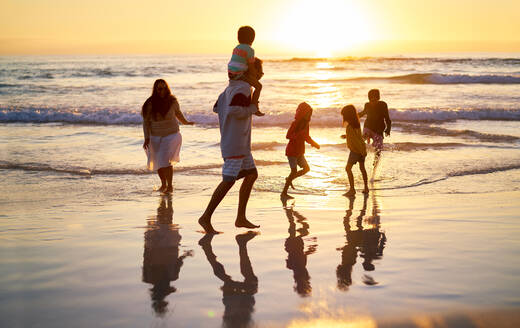 Familie watet in der Brandung an einem idyllischen Strand bei Sonnenuntergang - CAIF28243