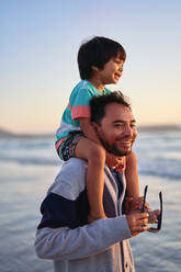 Glücklicher Vater trägt seinen Sohn auf den Schultern am Strand - CAIF28250