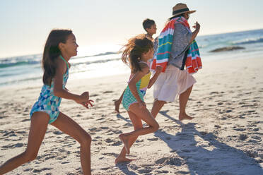 Playful family running on sunny ocean beach - CAIF28256