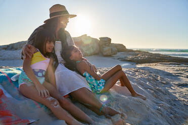 Mother and daughters relaxing on sunny beach - CAIF28257