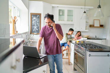 Mann arbeitet am Laptop in der Küche mit Kindern beim Essen - CAIF28278