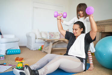 Daughter helping mother exercising with dumbbells in living room - CAIF28280