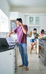 Vater arbeitet am Laptop in der Küche, während die Kinder essen - CAIF28306