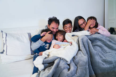 Glückliche Familie sieht sich einen Gruselfilm auf dem Wohnzimmersofa an - CAIF28328