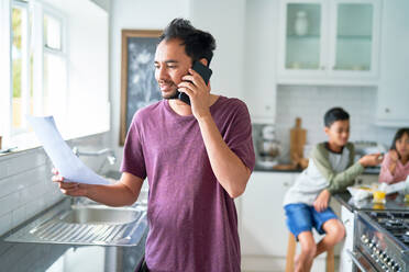 Vater telefoniert mit Smartphone in der Küche mit Kindern - CAIF28330