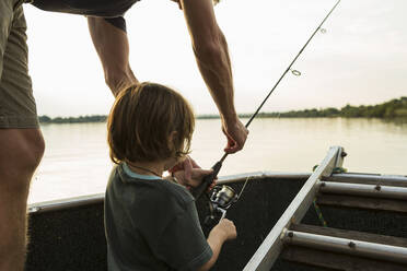 A five year old boy fishing from a boat on the Zambezi River, Botswana - MINF14564