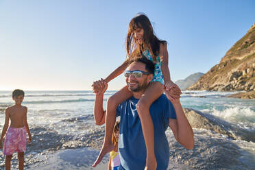 Glücklicher Vater trägt Tochter auf den Schultern am sonnigen Strand - CAIF28344