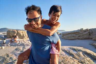 Happy father piggybacking son on sunny beach - CAIF28351