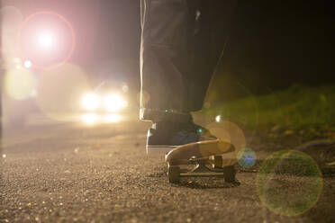 Young man skateboarding in headlights on roadside - CAIF28379