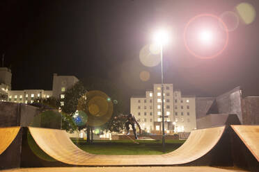 Junger Mann, der nachts auf der Rampe eines Skateparks Skateboard fährt - CAIF28382