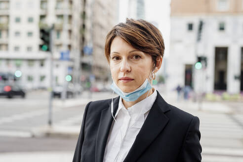 Close-up of confident businesswoman wearing mask against buildings in city - MEUF01207