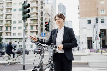 Weibliche Fachkraft hört Musik, während sie mit dem Fahrrad auf einer Straße in der Stadt spazieren geht - MEUF01212