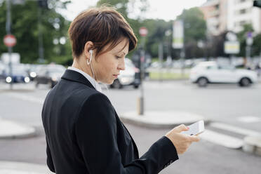 Nahaufnahme eines weiblichen Berufstätigen, der ein Smartphone benutzt, während er auf einer Straße in der Stadt steht - MEUF01218