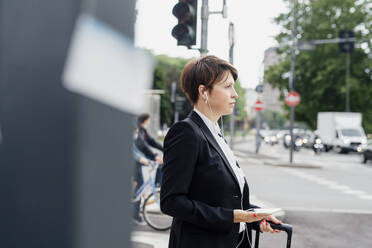 Geschäftsfrau hört Musik über Kopfhörer und schaut weg, während sie auf der Straße in der Stadt steht - MEUF01219