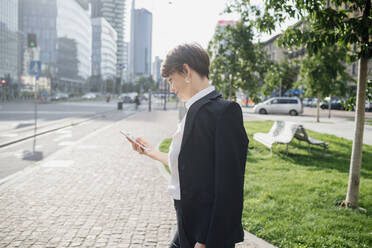 Female professional using mobile phone while standing on sidewalk in city - MEUF01233