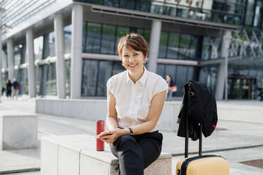 Smiling businesswoman with short hair sitting on seat against building in city - MEUF01244