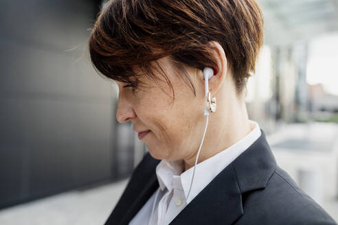 Nahaufnahme einer Geschäftsfrau mit kurzen Haaren, die über Kopfhörer Musik hört - MEUF01292