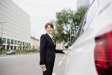 Lächelnde weibliche Fachkraft steht neben einem Auto auf der Straße in der Stadt - MEUF01297