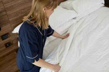 Zimmermädchen ordnet Bettdecke auf Bett in Hotelzimmer - ZEDF03475