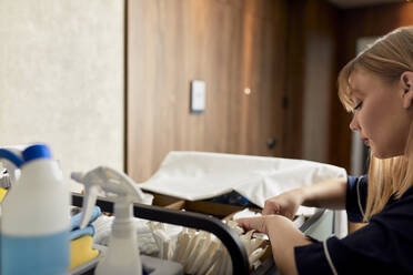 Nahaufnahme eines Zimmermädchens mit Reinigungsgeräten auf einem Rollwagen in einem Hotelflur - ZEDF03483