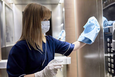 Close-up of chambermaid wearing mask cleaning elevator in hotel - ZEDF03496