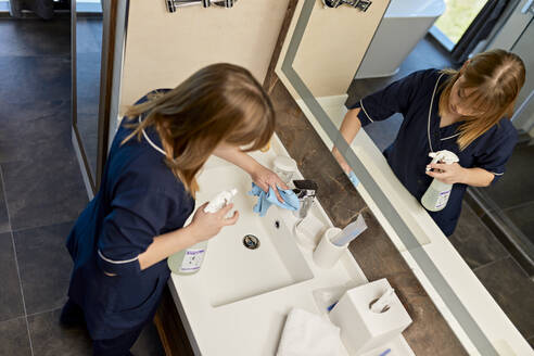 Chambermaid wiping faucet of bathroom sink in hotel - ZEDF03505