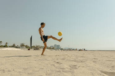 Hemdloser junger Mann spielt mit Ball am Strand gegen klaren Himmel an einem sonnigen Tag - VABF03116