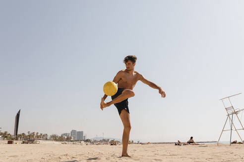 Hemdloser männlicher Sportler spielt mit Ball am Strand gegen klaren Himmel an einem sonnigen Tag - VABF03117