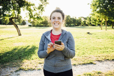Lächelnde Joggerin mit Smartphone im Park - SBAF00008