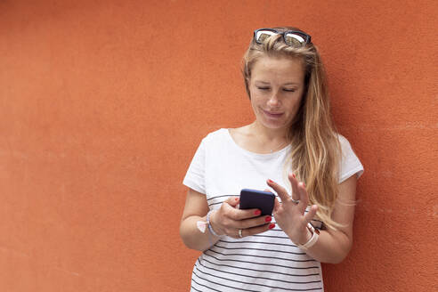 Mittlere erwachsene Frau, die ein Smartphone benutzt und sich an eine orangefarbene Wand lehnt - WPEF03180