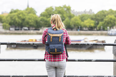 Mittlere erwachsene Frau, die einen Rucksack trägt und auf den Fluss schaut, während sie am Geländer steht - WPEF03192