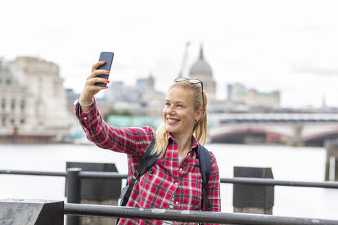 Lächelnde Frau, die ein Selfie mit ihrem Smartphone macht, während sie vor der St. Paul's Cathedral in der Stadt steht - WPEF03193