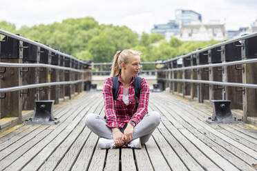 Mittlere erwachsene Frau mit kariertem Hemd schaut weg, während sie auf einer Brücke sitzt - WPEF03200
