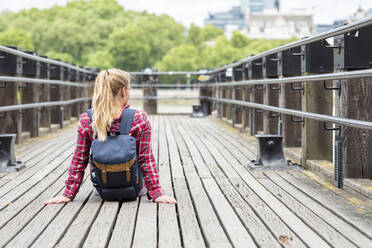 Mid adult woman with backpack sitting on bridge in city - WPEF03201