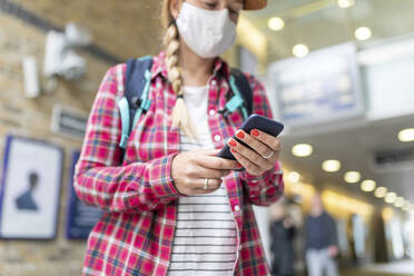 Nahaufnahme einer Frau mit Maske, die ein Smartphone benutzt, während sie an einer U-Bahn-Station steht - WPEF03208