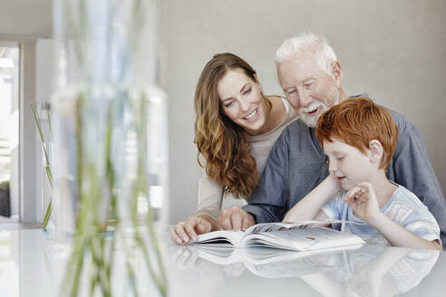Großvater, Mutter und Sohn lesen gemeinsam ein Buch in einer Villa - RORF02253