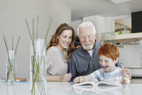 Glücklicher Großvater, Mutter und Sohn lesen ein Buch in einer Villa - RORF02254