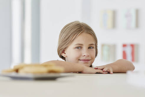 Porträt eines niedlichen Mädchens zu Hause mit Teller auf dem Tisch - RORF02264